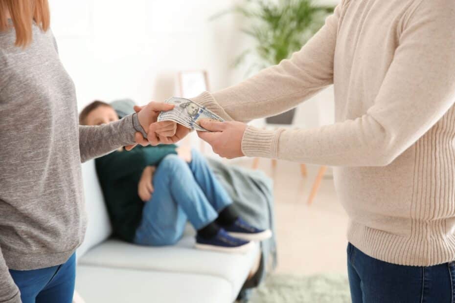 Ein Mann überreicht einer Frau einige Geldscheine, während im Hintergrund ein Kind auf einem Sofa sitzt, symbolisch für Unterhaltszahlungen.